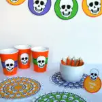Free printable skeleton Halloween table decorations - banner, cup wraps, food labels and doilies in orange, purple, green and yellow