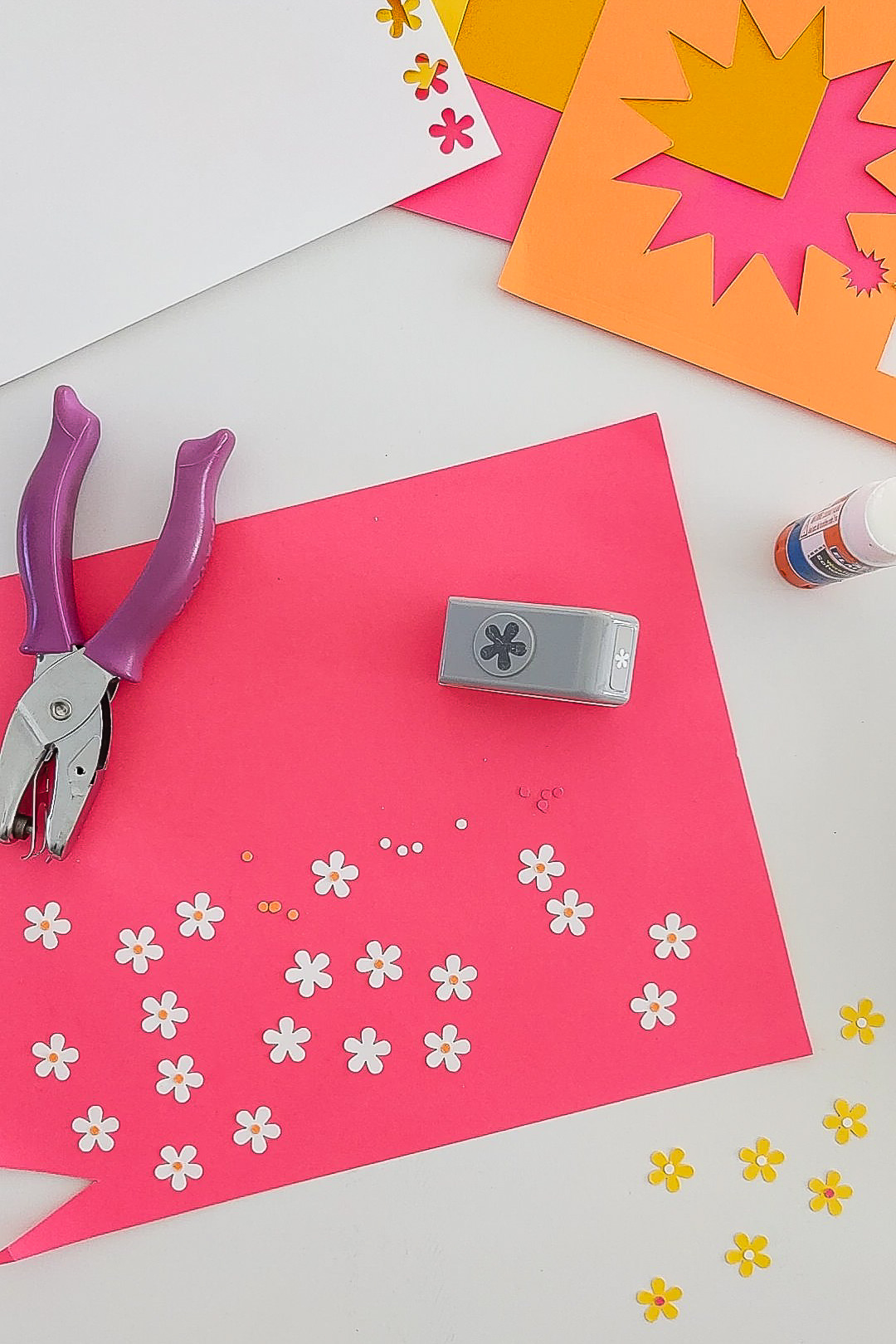 Flower paper punch, scrap paper, and paper flowers on a crafting table