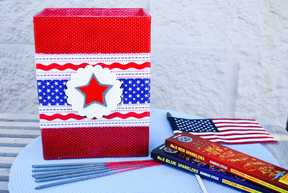 DIY safety sparkler caddy. Just fill with water and drop in hot used sparklers for NO sparkler burns this Fourth of July! Take a glass vase, decorate it with red, white and blue fabric and paper napkins using Mod Podge.