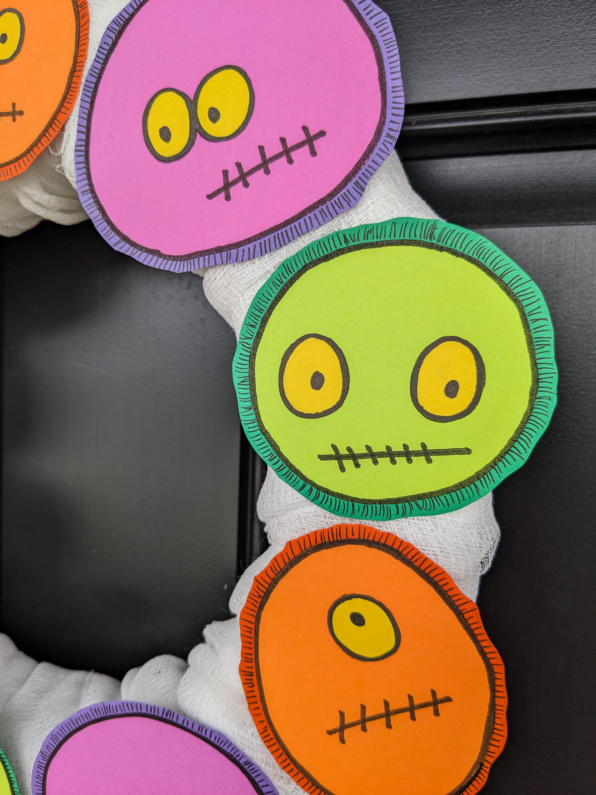 Green, purple, and orange monsters with yellow eyes on a Halloween front door wreath