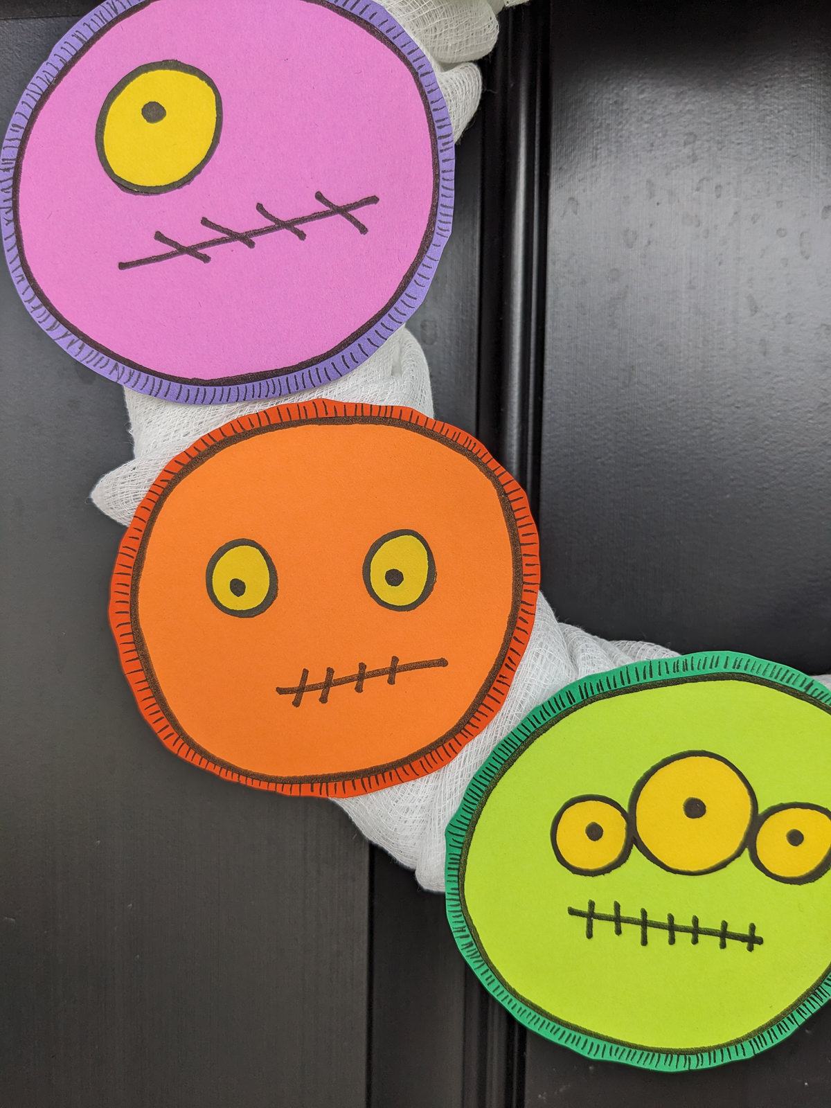 Green, purple, and orange monsters with yellow eyes on a Halloween front door wreath