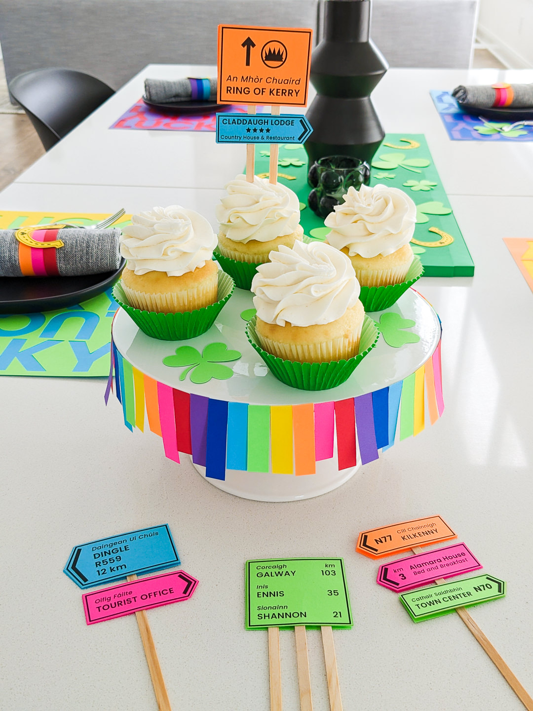 DIY Irish road signs cupcake toppers on a table next to cupcakes sitting on a rainbow cupcake stand