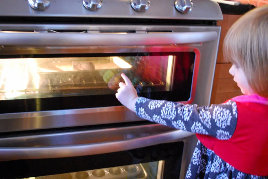 Girl watching shrinky dinks bake in the oven
